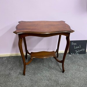 May include: A dark wood side table with a curved top and a lower shelf. The table has a delicate, ornate design and is in good condition.