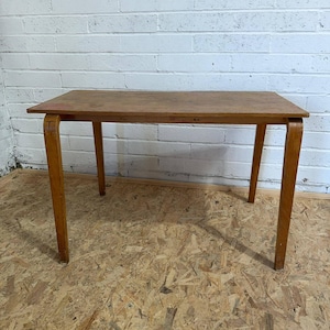 May include: A rectangular wooden table with a smooth, light brown finish. The table features a flat top surface and four sturdy, slightly curved legs that extend outward from the corners, providing a stable base for this functional furniture piece.