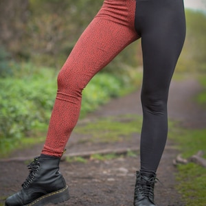 May include: Black and red leggings with a leopard print on one leg. The leggings are high-waisted and have a fitted silhouette. The person is wearing black boots.
