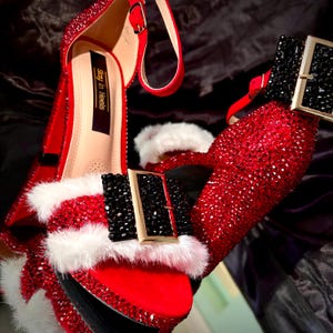 May include: Red high heels covered in sparkling rhinestones, with a platform sole and ankle strap. The shoes have a white faux fur trim and a black buckle. The words "Stay in Heels" are printed on the insole.