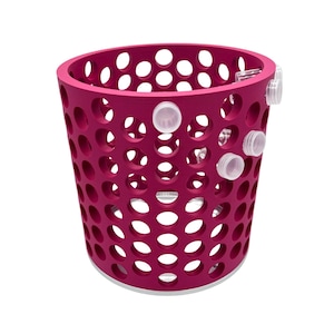 Könnte beinhalten: Ein magenta-farbener, zylindrischer Korb mit zahlreichen kreisförmigen Perforationen. Der Korb hat einen weißen Sockel und mehrere transparente, kreisförmige Aufsätze an der Seite. Das Design ist modern und funktional, geeignet für die Aufbewahrung oder dekorative Zwecke.