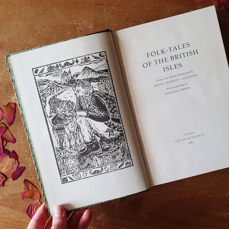 May include: An open book titled "FOLK-TALES OF THE BRITISH ISLES" with a black and white illustration on the left page. The illustration depicts a man and two figures in a landscape. The book's cover has a green and white patterned border.