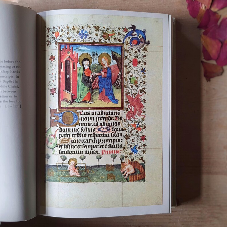 Może przedstawiać: Otwarta książka prezentuje kolorową średniowieczną ilustrację. Grafika przedstawia dwie postacie w szatach na tle budynku. Strona ozdobiona jest bogatymi kwiatowymi i liściastymi obramowaniami oraz ręcznie pisanym tekstem.