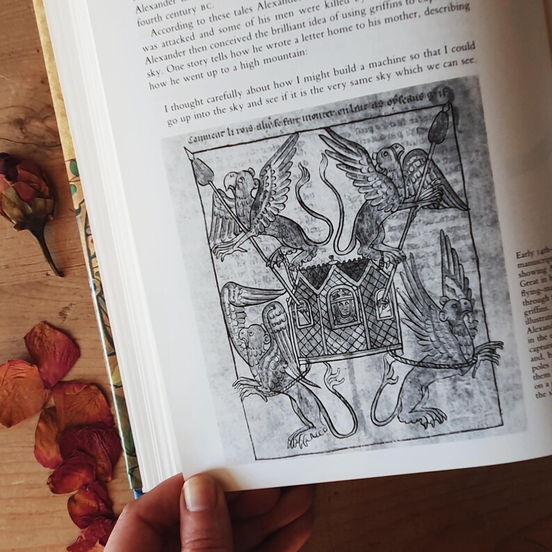 May include: An open book with a black and white illustration of a carriage being pulled by griffins. The illustration is from an old manuscript. The page also contains text in English.