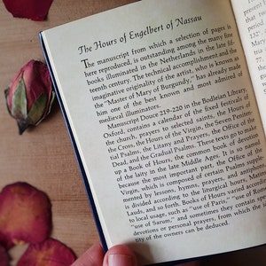 Puede incluir: Libro abierto con el t&iacute;tulo "The Hours of Engelbert of Nassau". El texto describe el origen del manuscrito en los Pa&iacute;ses Bajos a finales del siglo XV. El libro tiene una cubierta azul y est&aacute; sobre una superficie de madera.