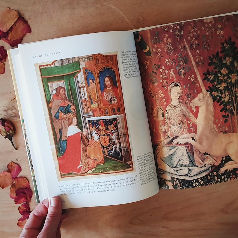 May include: An open book with illustrations of medieval art. One page features a colorful depiction of a royal ceremony, while the other showcases a tapestry with a woman and a unicorn. The book is titled "Mythical Beasts".