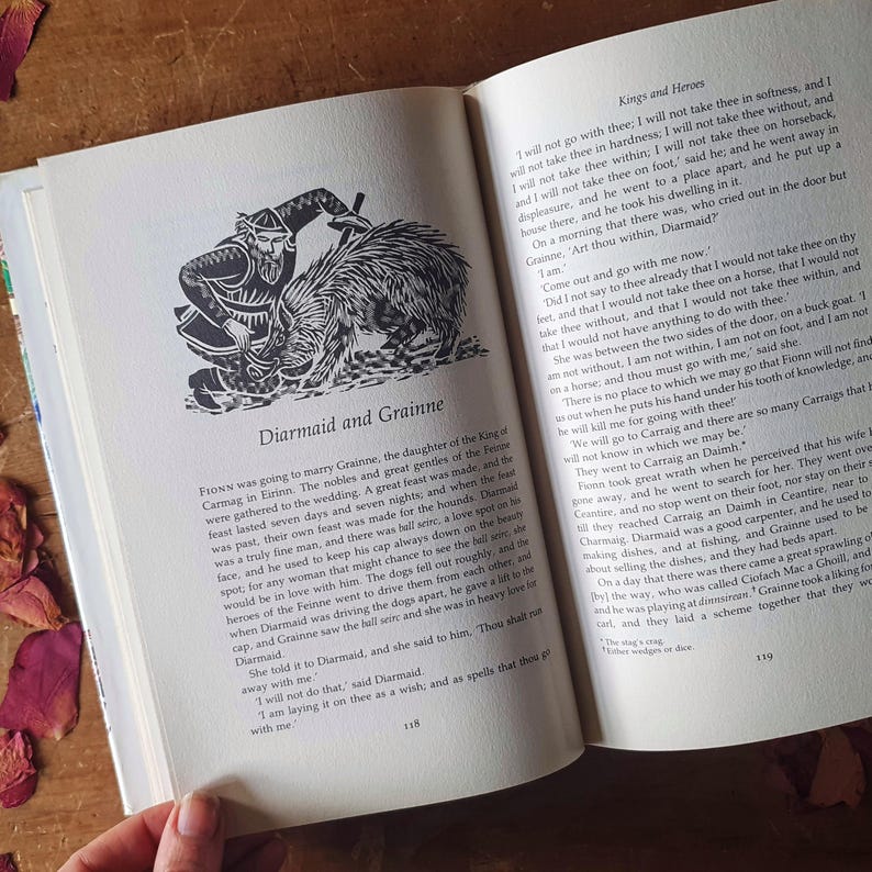May include: Open book with text and a black and white illustration of a man with a sword and a creature. The text reads "Diarmaid and Grainne" and details a story about a wedding and a love affair. The pages are off-white.