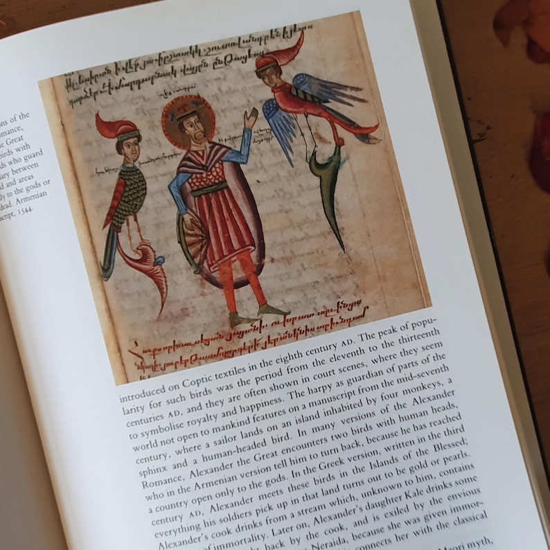 May include: A page from an antique book featuring a colorful illustration. The artwork depicts a man with a halo, flanked by two bird-like figures. The figures are in red, blue, and green, with the man in red and blue attire. Text surrounds the illustration.