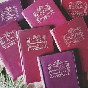 May include: A collection of eight vintage hardback books by Thomas Hardy, all with burgundy covers and gold lettering. The titles include "The Trumpet Major", "The Woodlanders", "A Group of Noble Dames", "Tess of the D'Urbervilles", "Life's Little Ironies", "The Return of the Native", and "The Well-Beloved".