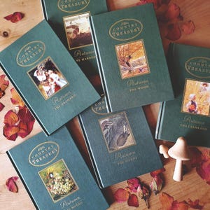 May include: A selection of teal-covered hardback books with gold lettering. Each book displays an autumn-themed illustration within a rectangular frame. Titles include "Country Treasury" and "Autumn" with location names like "The Orchard".