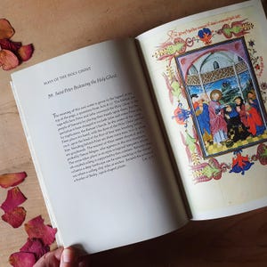 Może przedstawiać: Otwarta książka z tytułem "MASS OF THE HOLY GHOST" i kolorową ilustracją sceny religijnej. Obraz przedstawia postacie w szatach i dekoracyjną obw&oacute;dkę. Suche płatki r&oacute;ż są rozrzucone wok&oacute;ł książki.