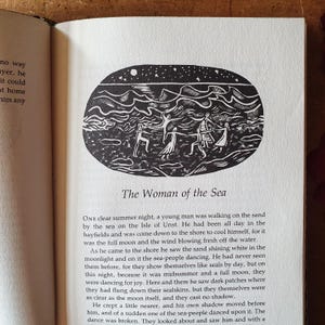 May include: A black and white illustration from a book, depicting a scene with figures dancing under a starry sky. The text "The Woman of the Sea" is below the image, set against a white page.