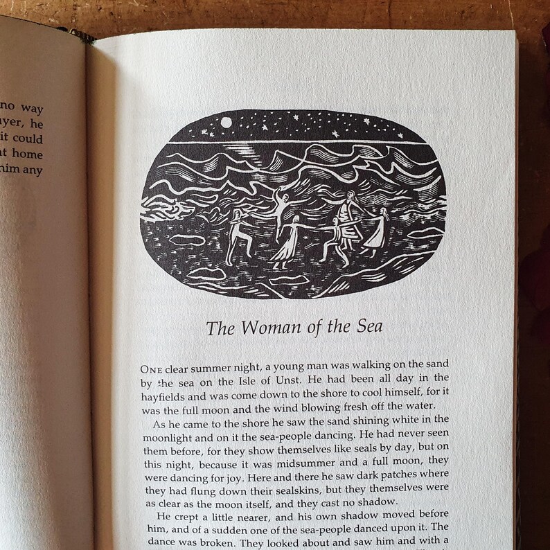 May include: A black and white illustration from a book, depicting a scene with figures dancing under a starry sky. The text "The Woman of the Sea" is below the image, set against a white page.