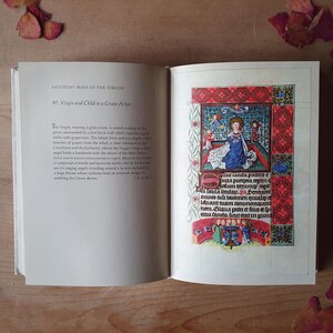 Może przedstawiać: Otwarta książka z tytułem "Saturday Mass of the Virgin" i szczeg&oacute;łową ilustracją Dziewicy i Dzieciątka w altanie z winogronami. Ilustracja zawiera żywe kolory i skomplikowane detale, z tekstem na obu stronach.