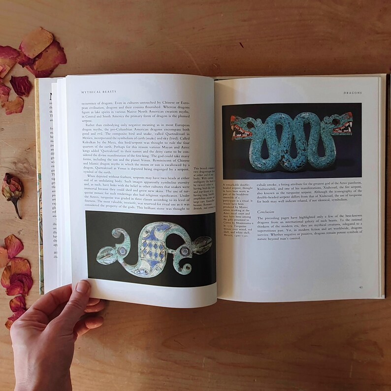 May include: An open book displaying images of ancient artifacts. One image shows a turquoise serpent with red accents, while another depicts a blue and white stylized serpent. The page is titled "Mythical Beasts."