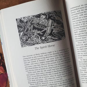 May include: A black and white illustration titled "The Spirit Horse" on a book page. The image depicts a person riding a horse, with text below describing the story. The book is open, with text on the adjacent page.