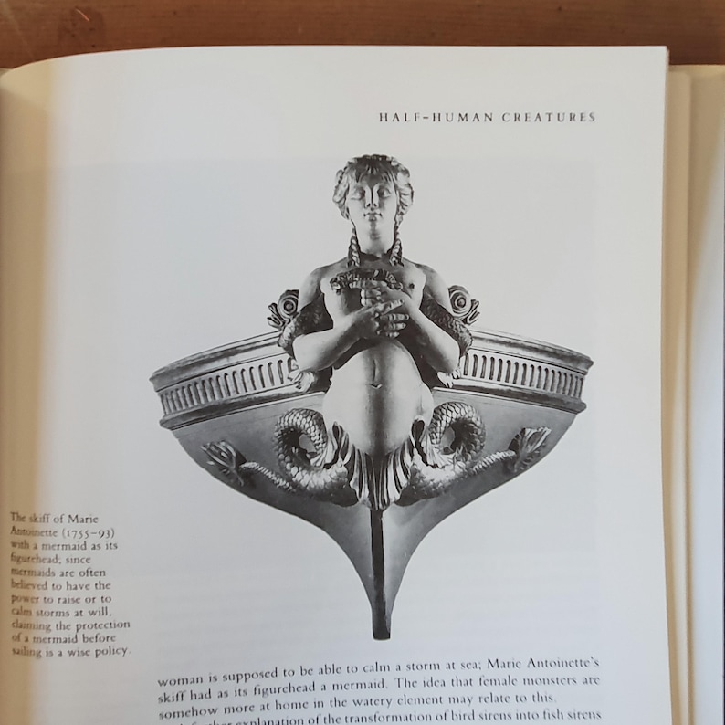 May include: A grayscale illustration from a book depicting a mermaid figurehead on a boat. The text "HALF-HUMAN CREATURES" is at the top. The mermaid has a human upper body and a fish tail, with decorative elements.
