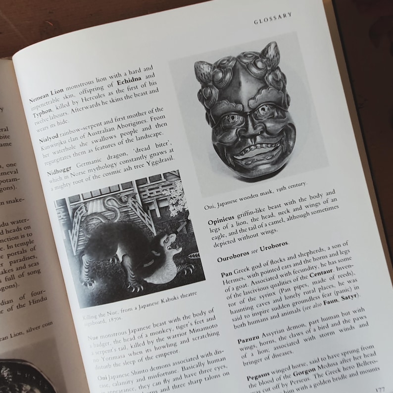 May include: A page from a book featuring a black and white image of a Japanese wooden mask from the 19th century. The mask has a detailed face with a wide grin and is surrounded by text.