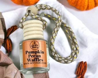 May include: A clear glass air freshener bottle with a wooden cap and a braided cord. The label reads "Pumpkin Pecan Waffles" and "Lil Wax Bakery". The background includes orange pumpkins and pecans.