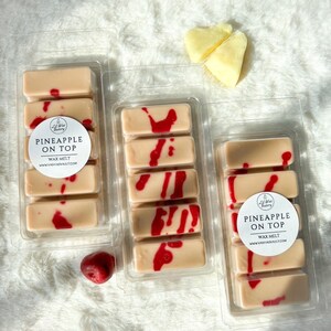 May include: Three clear plastic containers with wax melts inside. Each container has four wax melts, and the wax melts are a light brown color with red swirls. The containers have a white label with the text "PINEAPPLE ON TOP WAX MELT WWW.VASHIASVAULT.COM".