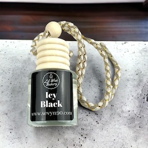 May include: A clear glass bottle with a black label that says "Lil Wax Bakery" and "Icy Black" with the website "www.sevyvn90.com". The bottle has a wooden cap with a gold and white braided string attached.