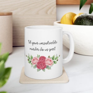 May include: White ceramic mug with a pink floral design and the text "Til your unsolvable murder do us part".