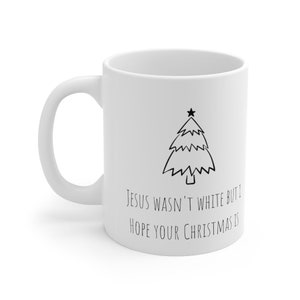 May include: White ceramic mug with a black outline of a Christmas tree and the text "Jesus wasn't white but I hope your Christmas is".