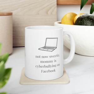 May include: White ceramic mug with a black outline of a laptop and the text "not now sweetie. mommy is cyberbullying on Facebook".