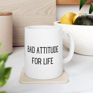 May include: White ceramic coffee mug with black text that reads "Bad Attitude For Life".