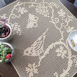May include: A beige crocheted table runner with a delicate floral pattern. The runner is made of fine yarn and has a delicate, lacy texture.