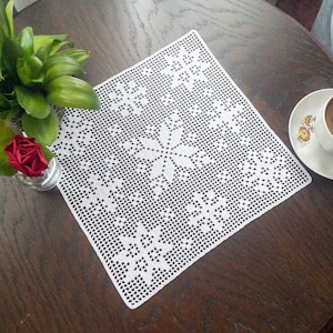 以下が含まれることがあります： 中央に花柄の白いレースのドイリー。ドイリーは濃い木製のテーブルの上に置かれています。