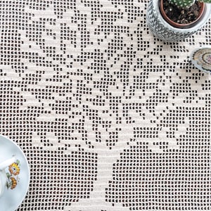 May include: A white crocheted tablecloth with a tree design. The tablecloth is on a brown wooden surface.