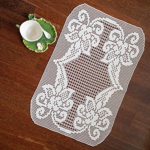 May include: White crocheted doily with a star-shaped design. The doily is made of delicate, intricate stitches and has a scalloped edge.