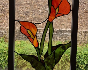 May include: A stained glass window featuring three orange calla lilies with green leaves. The window is framed in a brown wood frame.