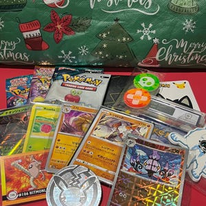 May include: A selection of Pokémon trading cards, packs, and merchandise, including a silver coin, stickers, and colorful game cards. The background features a green Christmas-themed gift bag with holiday decorations and the words "Merry Christmas."