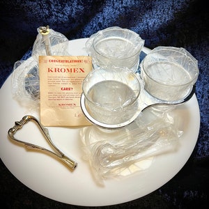 May include: A white serving tray with a silver handle and three clear glass bowls. The bowls are wrapped in plastic and the tray is on a white surface. The image includes a small card with the text "Congratulations! Kromex" and "Care? Easy! To clean this gleaming beauty, simply wipe with a soft damp cloth thoroughly. Do not use harsh abrasive scouring agents in cleaning. Kromex".