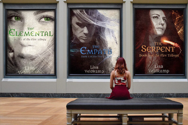 Op de afbeelding: Drie boekomslagen die in een galerie worden tentoongesteld. De omslagen tonen het gezicht van een vrouw met een dramatische achtergrond. De titels zijn "The Elemental", "The Empath" en "The Serpent". Elk boek maakt deel uit van een trilogie genaamd "The Fire Trilogy".