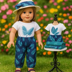 Puede incluir: Una muñeca vestida con una camiseta blanca y pantalones azules, ambos con un estampado de hojas turquesas. La muñeca también lleva un sombrero a juego. Un segundo conjunto, con una falda y toallas dobladas, se exhibe en un maniquí. El fondo es un jardín colorido.