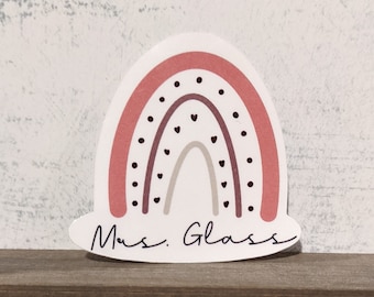 May include: A pink, brown, and beige rainbow sticker with black polka dots and small hearts. The sticker has the text "Mrs. Glass" written in cursive.