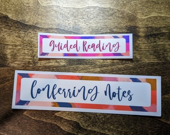 Könnte beinhalten: Zwei rechteckige Aufkleber mit weißen Textfeldern. Der obere Aufkleber lautet "Guided Reading" in rosa Schrift. Der untere Aufkleber lautet "Conferring Notes" in blauer Schrift. Beide haben farbenfrohe abstrakte Ränder.