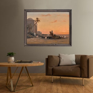 a framed picture of the artwork called Halt by the Well; by August Veillon. The image is of arab men and their camels in the desert next to a well and buildings.