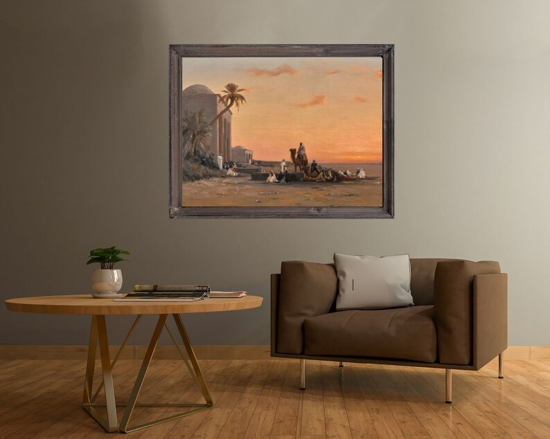 a framed picture of the artwork called Halt by the Well; by August Veillon. The image is of arab men and their camels in the desert next to a well and buildings.