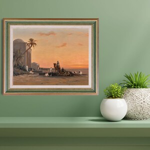 a framed picture of the artwork called Halt by the Well; by August Veillon. The image is of arab men and their camels in the desert next to a well and buildings.