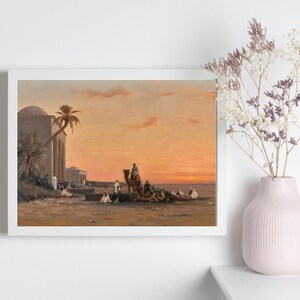 a framed picture of the artwork called Halt by the Well; by August Veillon. The image is of arab men and their camels in the desert next to a well and buildings.