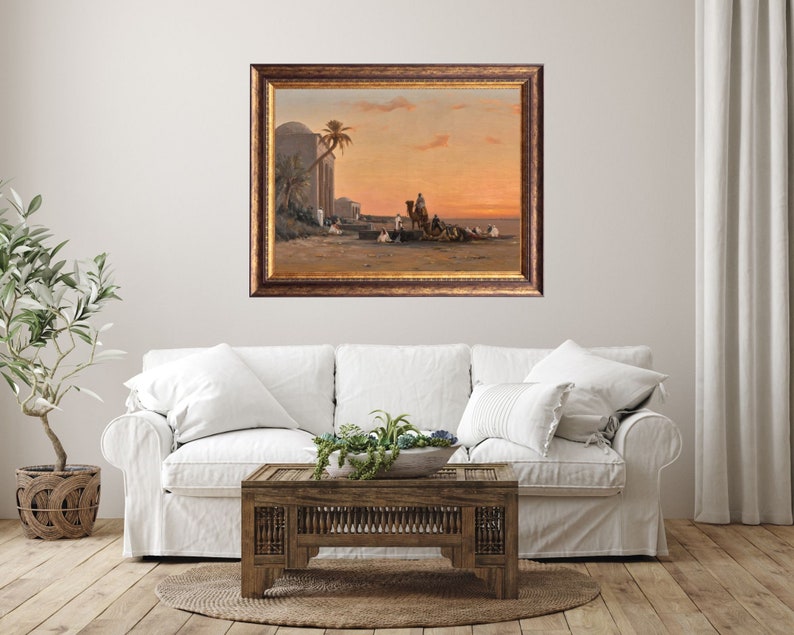 a framed picture of the artwork called Halt by the Well; by August Veillon. The image is of arab men and their camels in the desert next to a well and buildings.