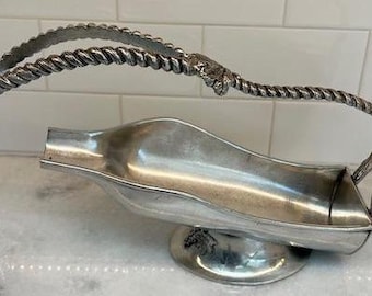 May include: Silver wine bottle holder with a twisted rope handle. The holder is shaped like a bottle and has a base.