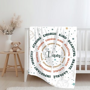 Puede incluir: Manta de bebé blanca con un diseño circular de afirmaciones positivas en texto verde y naranja. El texto dice "Yo soy" en el centro, rodeado de "capaz, valiente, hermoso, amable, suficiente, fuerte, valioso, importante".