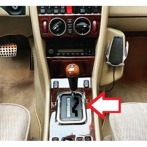 May include: Interior view of a classic car's center console. The image highlights the gear shift lever with a wooden knob, surrounded by a chrome frame. The console features wood paneling, buttons, and a radio.