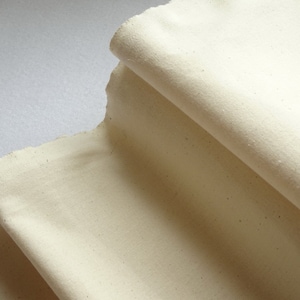 May include: A close-up of a folded piece of off-white fabric. The fabric has a slightly textured surface and appears to be natural cotton.