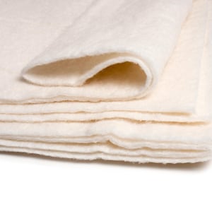 May include: A stack of white cotton batting, folded in half, with the edges of the layers visible.